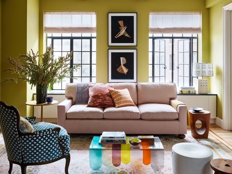 a living room with a pink sofa and a coloful glass coffee table and a blue and white armchair and tall french doors at the back and chartreuse painted walls