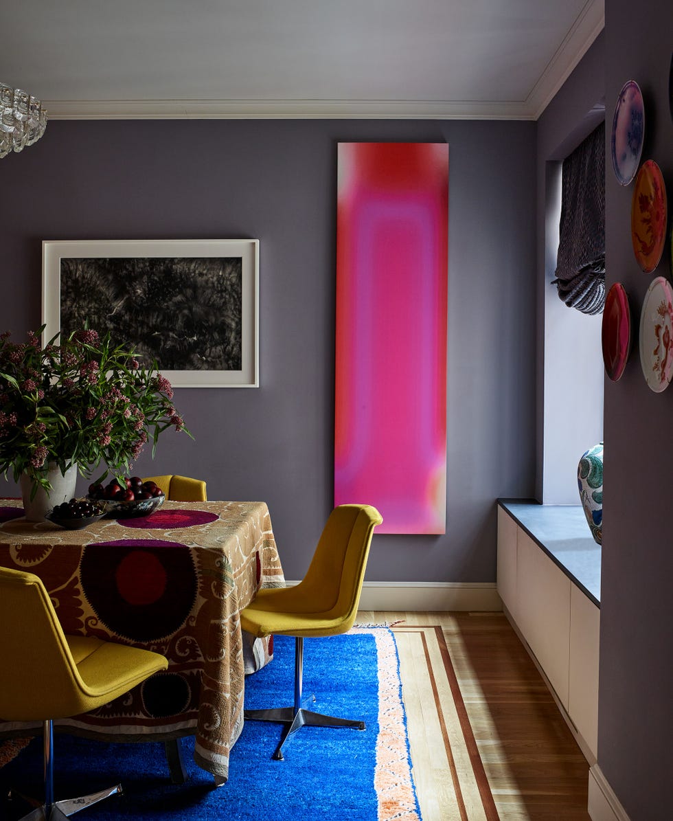 long pink artwork on a dusky purple wall with a draped table in front with yellow swivel chairs pulled up to it
