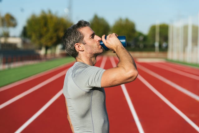 mature fitness man on red running track, drinking from blue bottle, wearing gray t shirt. copy space. copy space. close up. lifestyle and sports
