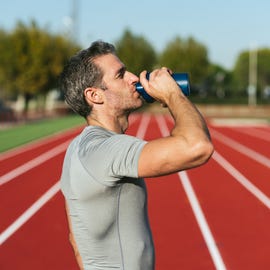 mature fitness man on red running track, drinking from blue bottle, wearing gray t shirt. copy space. copy space. close up. lifestyle and sports mature fitness man on red running track, drinking from blue bottle, wearing gray t shirt. copy space. copy space. close up. lifestyle and sports