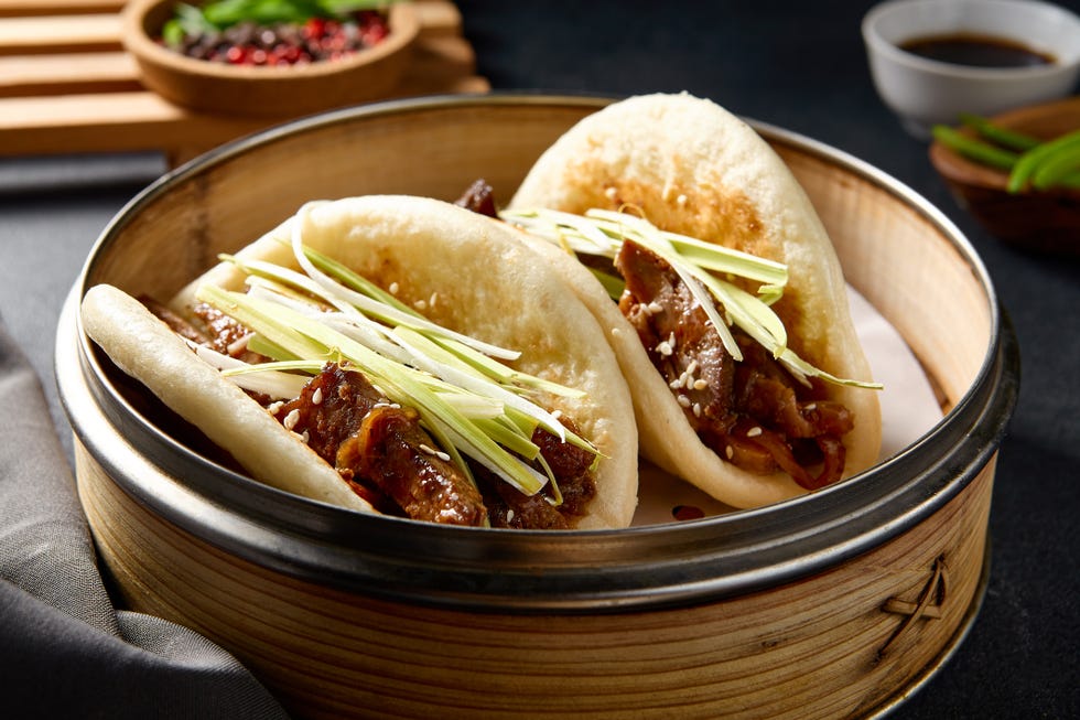 elegant presentation of peking duck bao buns garnished with fresh green onions, in traditional bamboo steamers