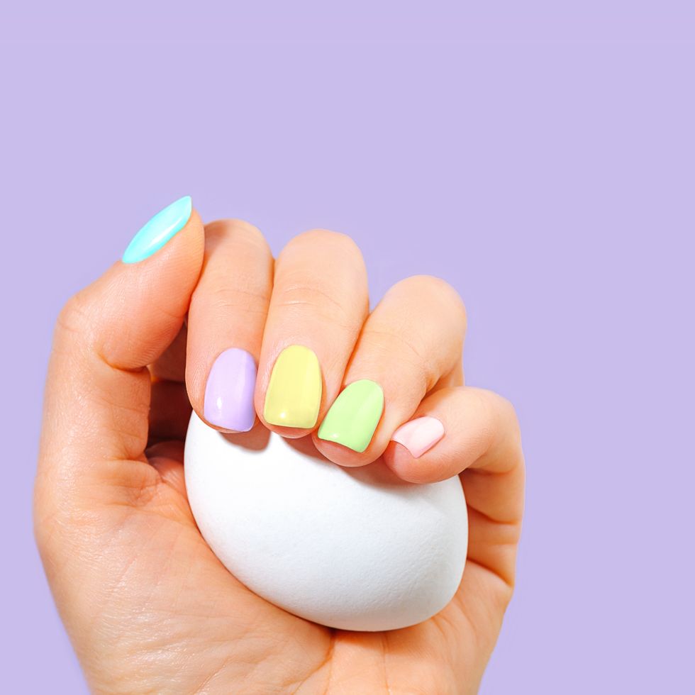 elegant woman's hand with pastel color manicure holding a white egg on easter holiday on trendy color of the year 2022 very peri purple violet lavender color background