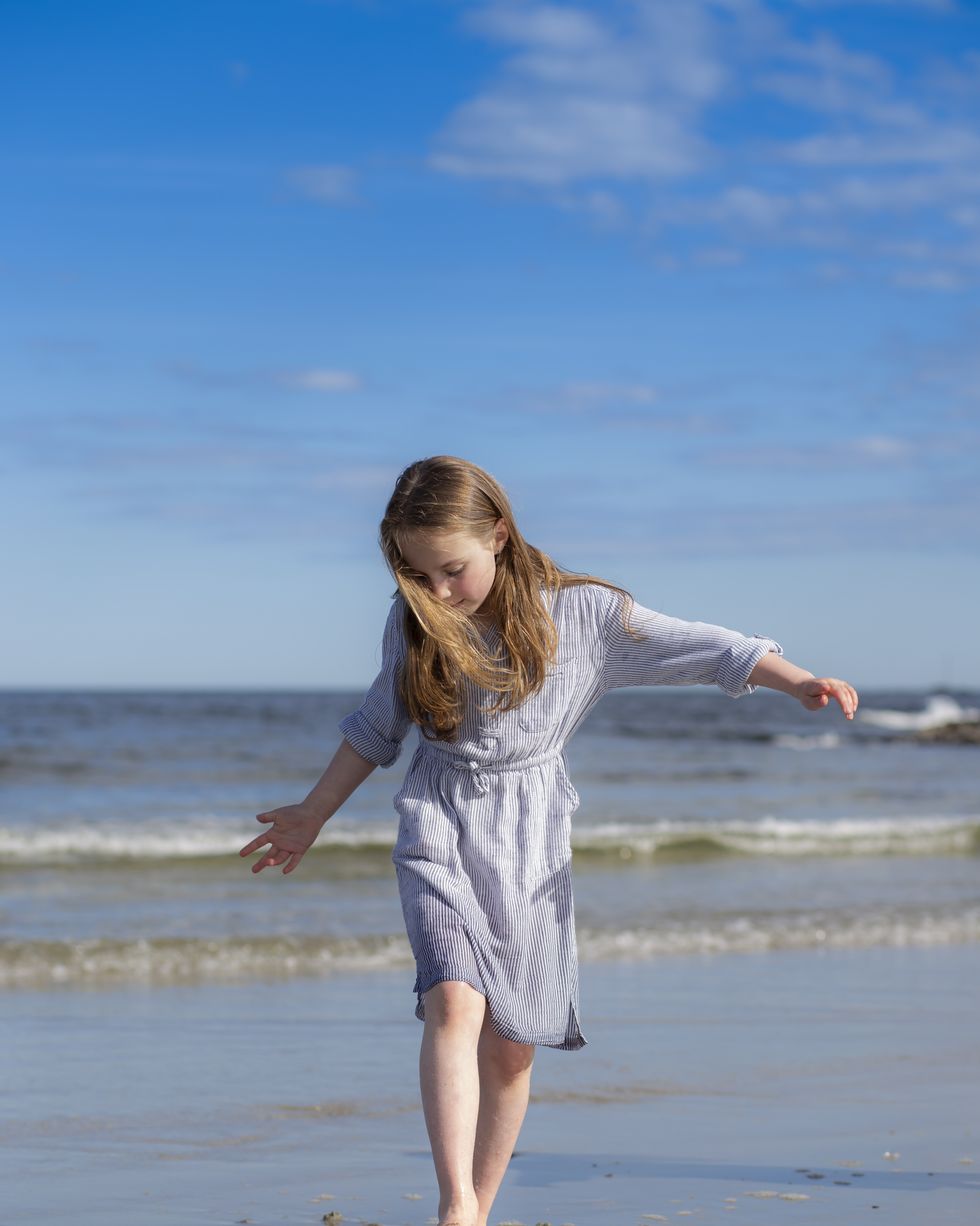 elementary age girl in blue dress walking on a beach and digging feet into the sand
