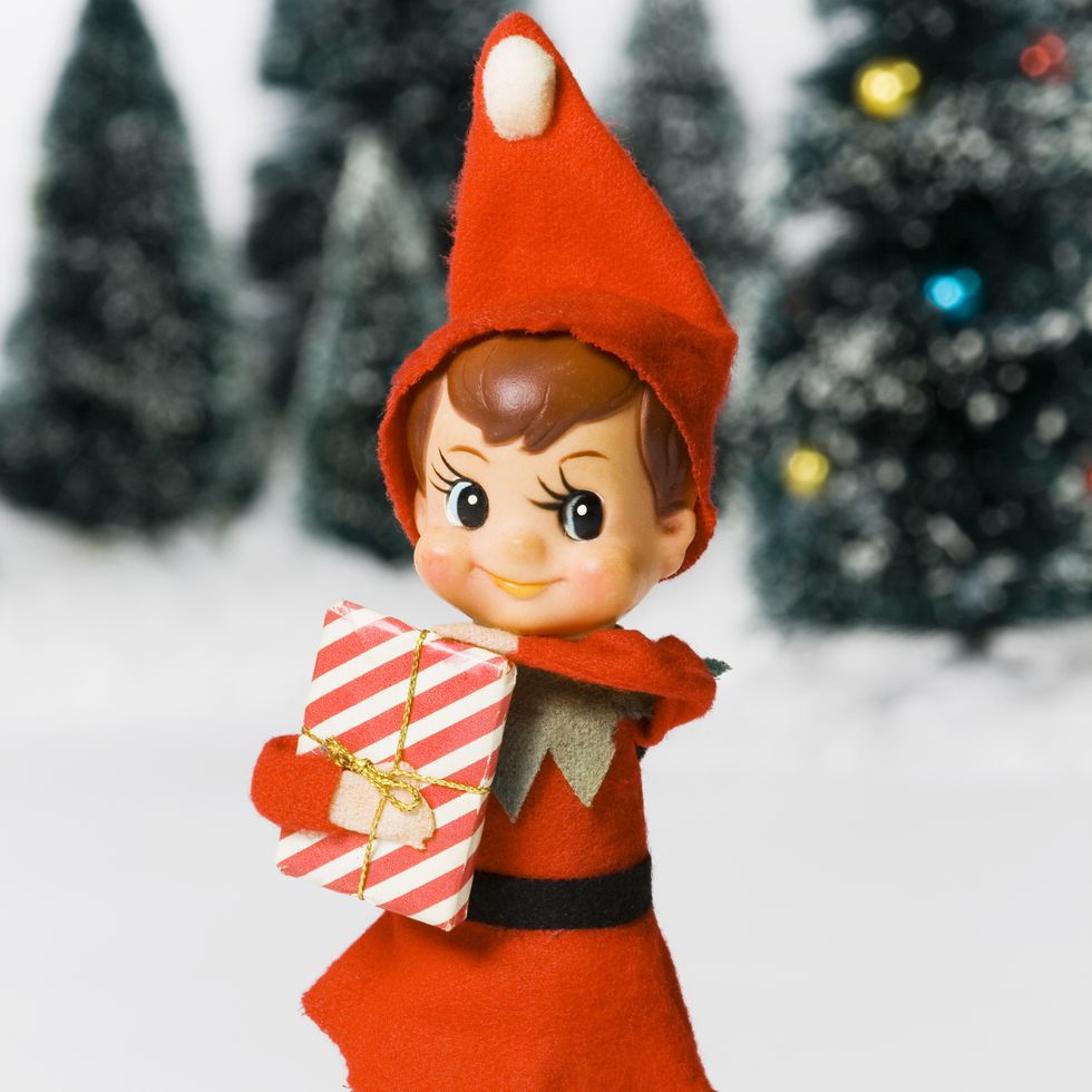 elf on the shelf holding present standing in snow