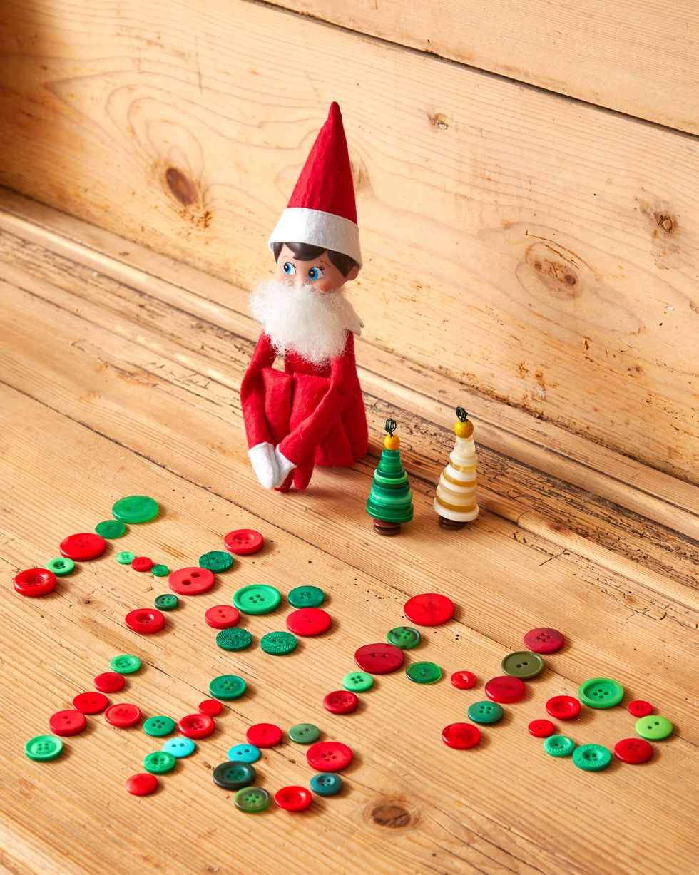 elf on the shelf with tiny christmas trees made from stacked buttons, red and green buttons spell out ho ho ho