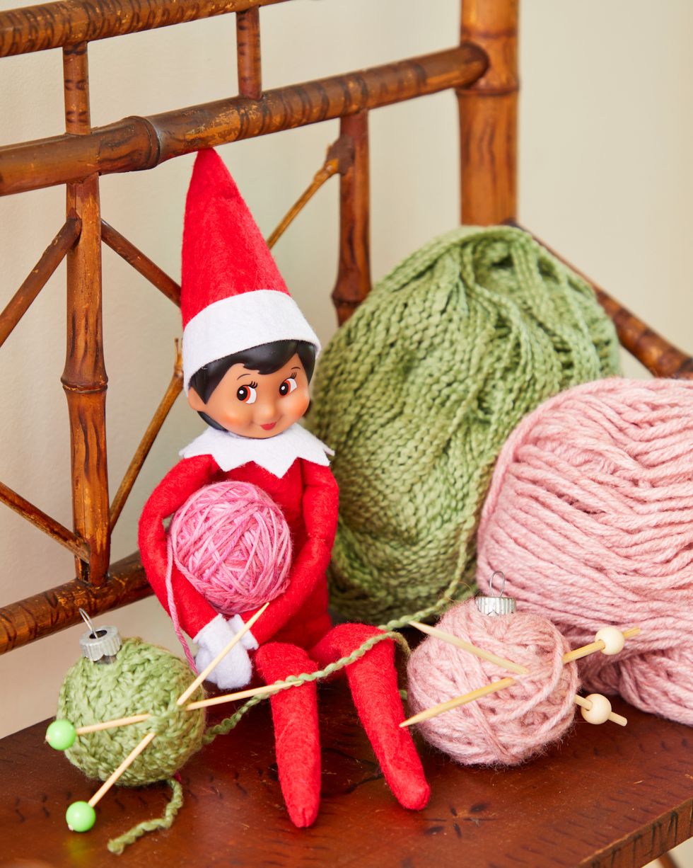 elf on the shelf on bench with balls of yarn and christmas ornaments made to look like balls of yarn