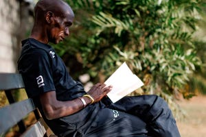 eliud kipchoge leyendo un libro sentado en un banco