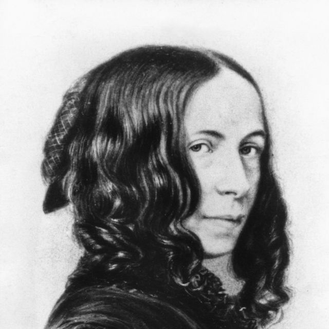 a woman facing to the right looks over her right shoulder to stare at the camera, she wears a dress and curls in her hair