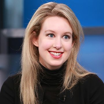 elizabeth holmes smiles and looks past the camera, she is wearing a black turtleneck and red lipstick