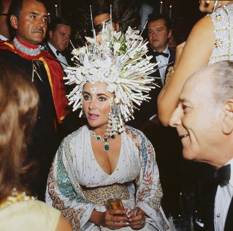 september 1967  english movie star elizabeth taylor attends a social function wearing an elaborate headdress of pearls and fake flowers, a jewelled dress and an emerald necklace  photo by keystonegetty images