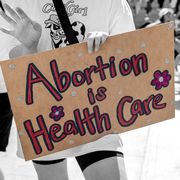one protest sign on the left that reads pray to end abortion and one on the right that reads abortion is health care