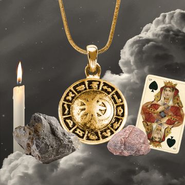 a gold and silver pendant with a candle and a stone on a cloudy day