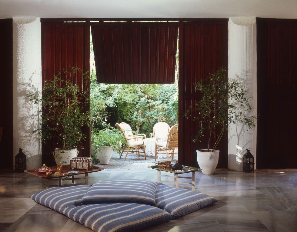 a living room with a large window and large blue and white striped cushions on the floor and potted plants and low tables