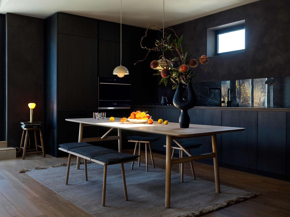 a dark kitchen with black cabinets and a long wooden dining room table