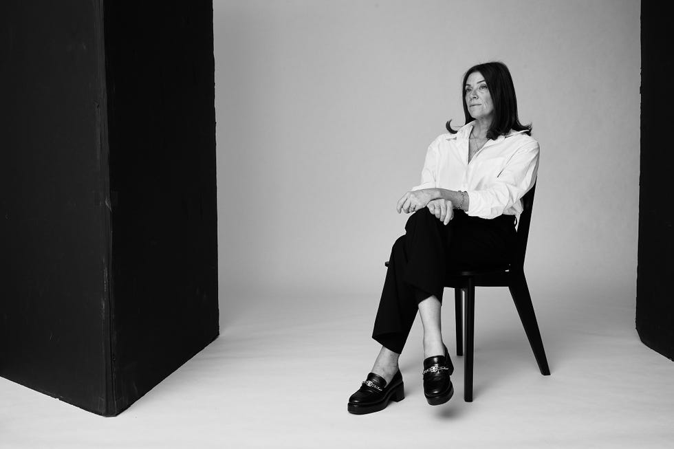 an individual sits on a black chair in a studio wearing a white shirt and black trousers their arms are casually crossed and they wear stylish black shoes the background features a stark contrast of dark and light elements enhancing the minimalist atmosphere shadows and lighting emphasize the simplicity of the scene