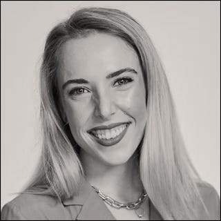 a person with long blonde hair wearing a chain necklace against a neutral background