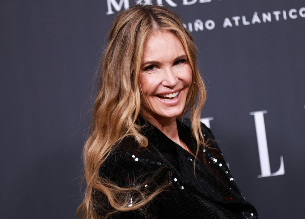 elle macpherson smiling in front of a red carpet backdrop