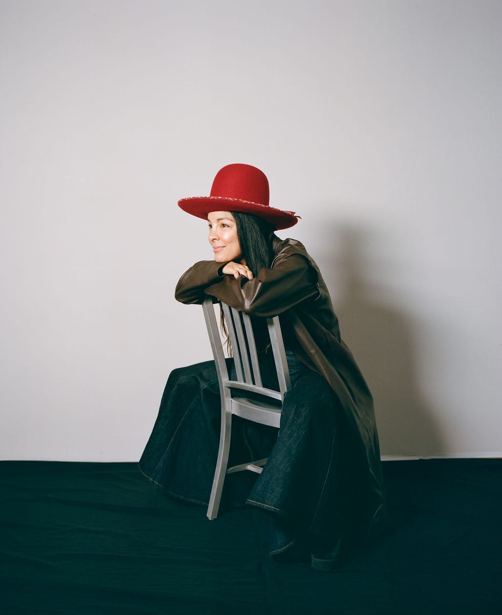 a person wearing a red hat and brown coat sitting on a white chair with denim pants