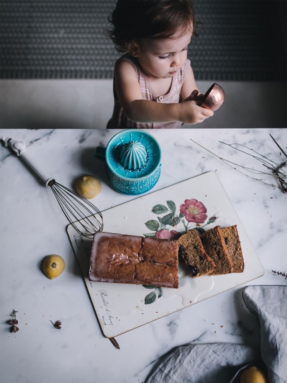 niña pequeña con una cuchara medidora de cocina frente a un bizcocho de limón
