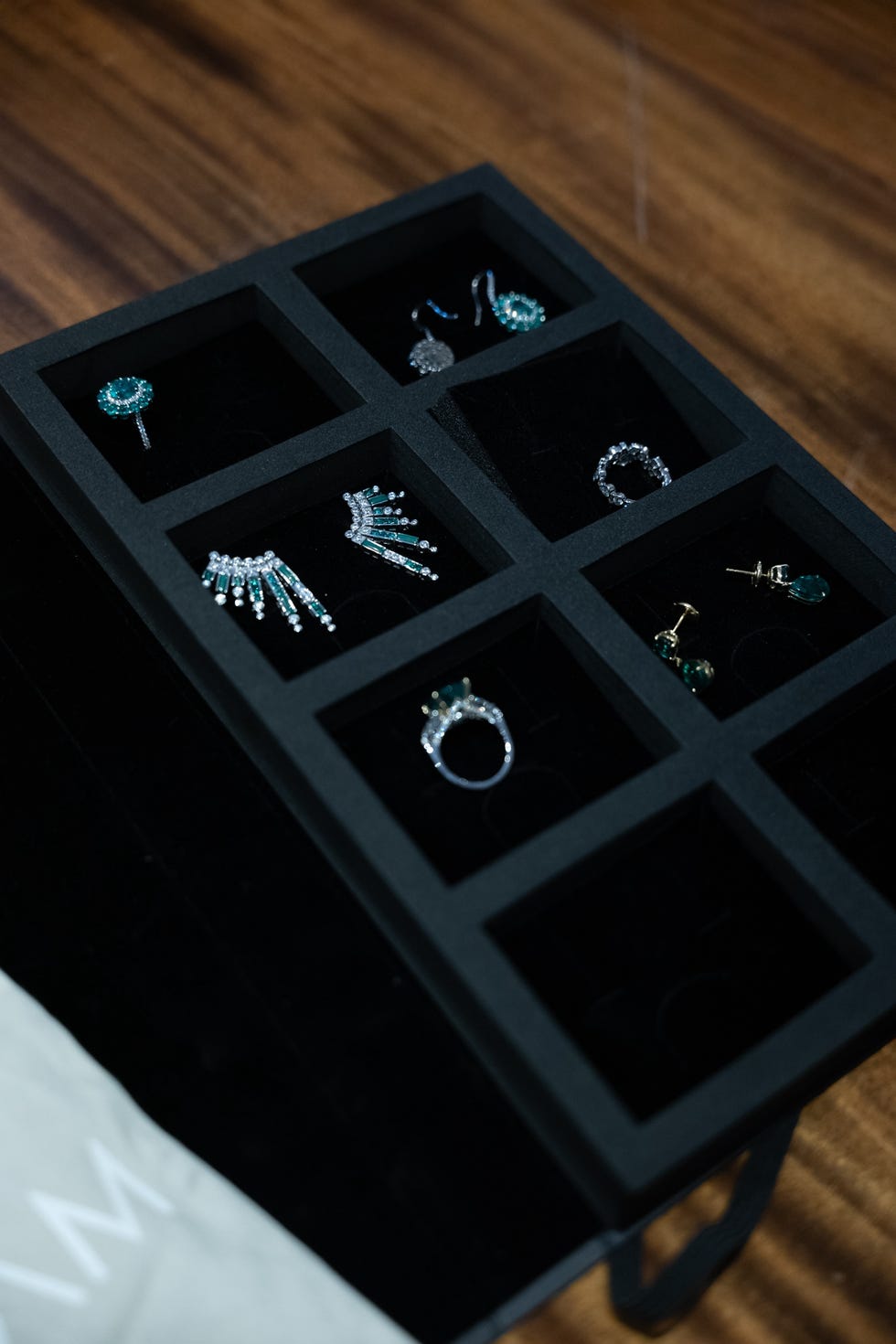 a black jewelry box features six compartments filled with different jewelry pieces items include rings, earrings, and a decorative hairpiece the jewelry has a combination of silver and turquoise tones, with sparkling accents the box itself is set against a dark wooden surface, highlighting the elegance of the accessories