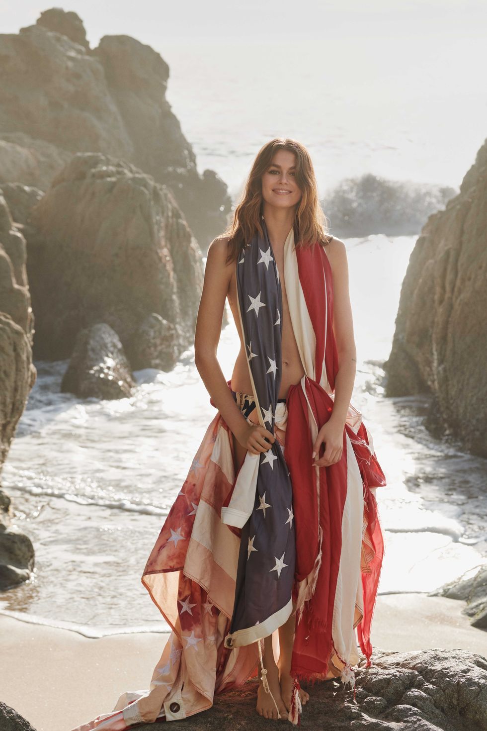 a white brunette woman stands on a beach shoreline wearing an american flag gown