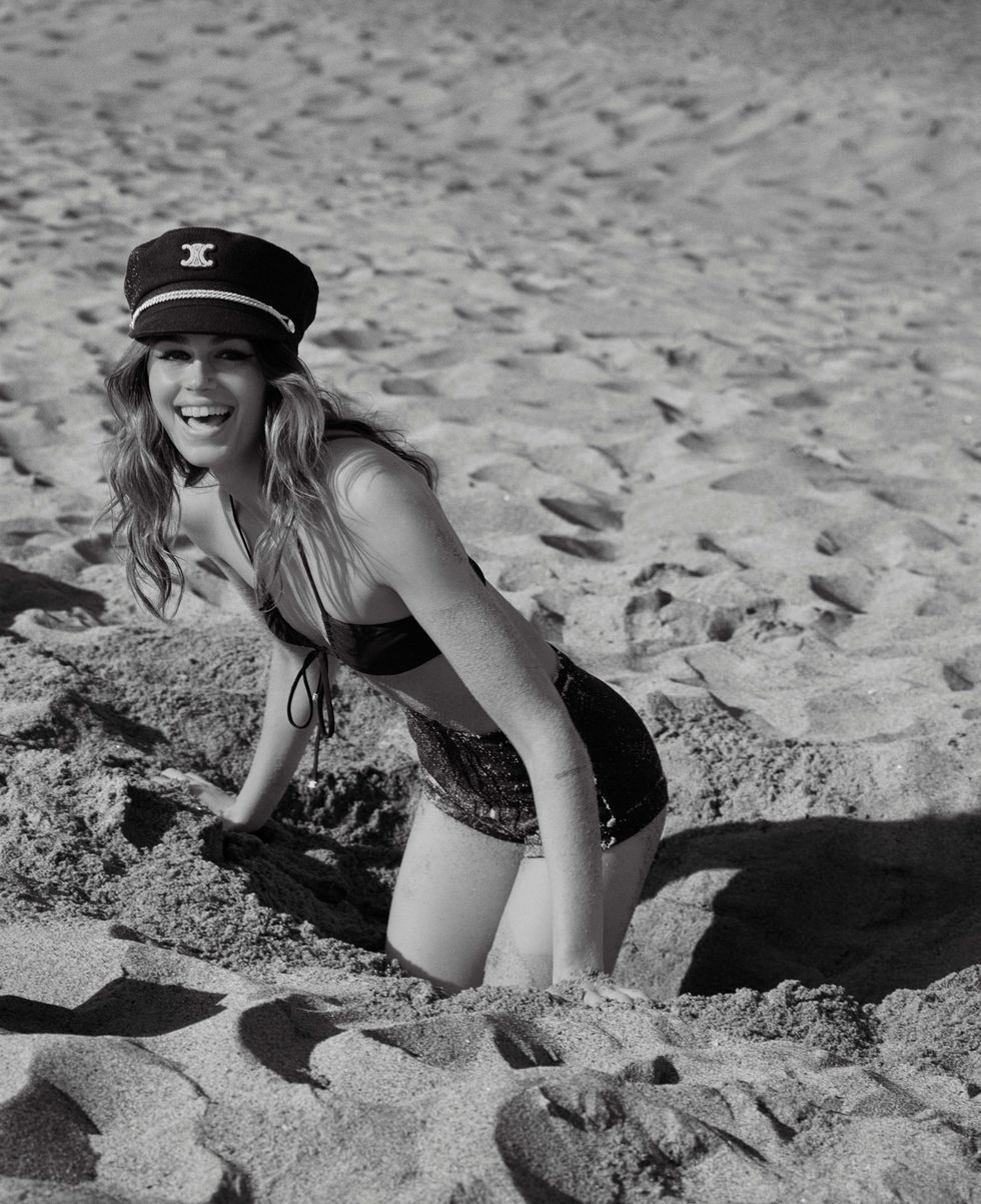 a white brunette woman wearing a black bikini and hat and posing in the sand