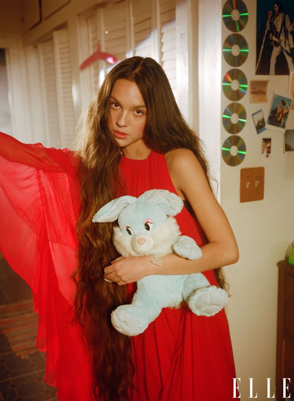 olivia rodrigo, in a diaphopnous red ball gown, clutches a pale blue stuffed bunny