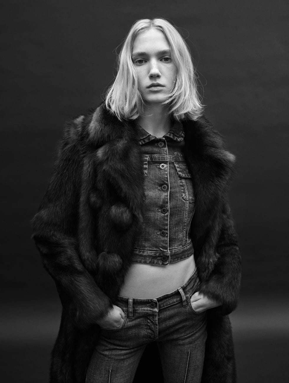 a woman with a blond bob wearing a crop top, jeans and a jacket