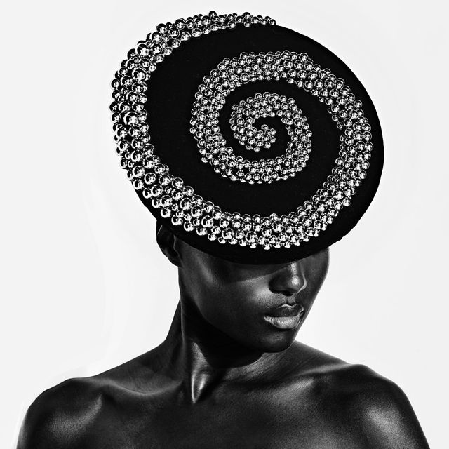 a black and white image of a black woman wearing an embellished silver and black hat
