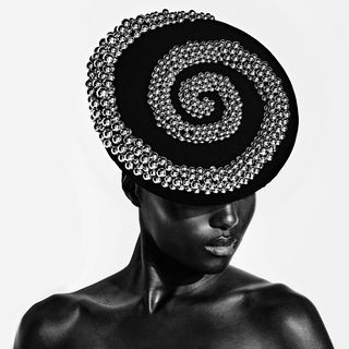 a black and white image of a black woman wearing an embellished silver and black hat