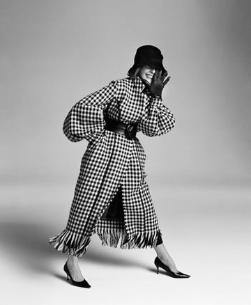 a woman in a houndstooth coat and black hat, raising her hand to her face