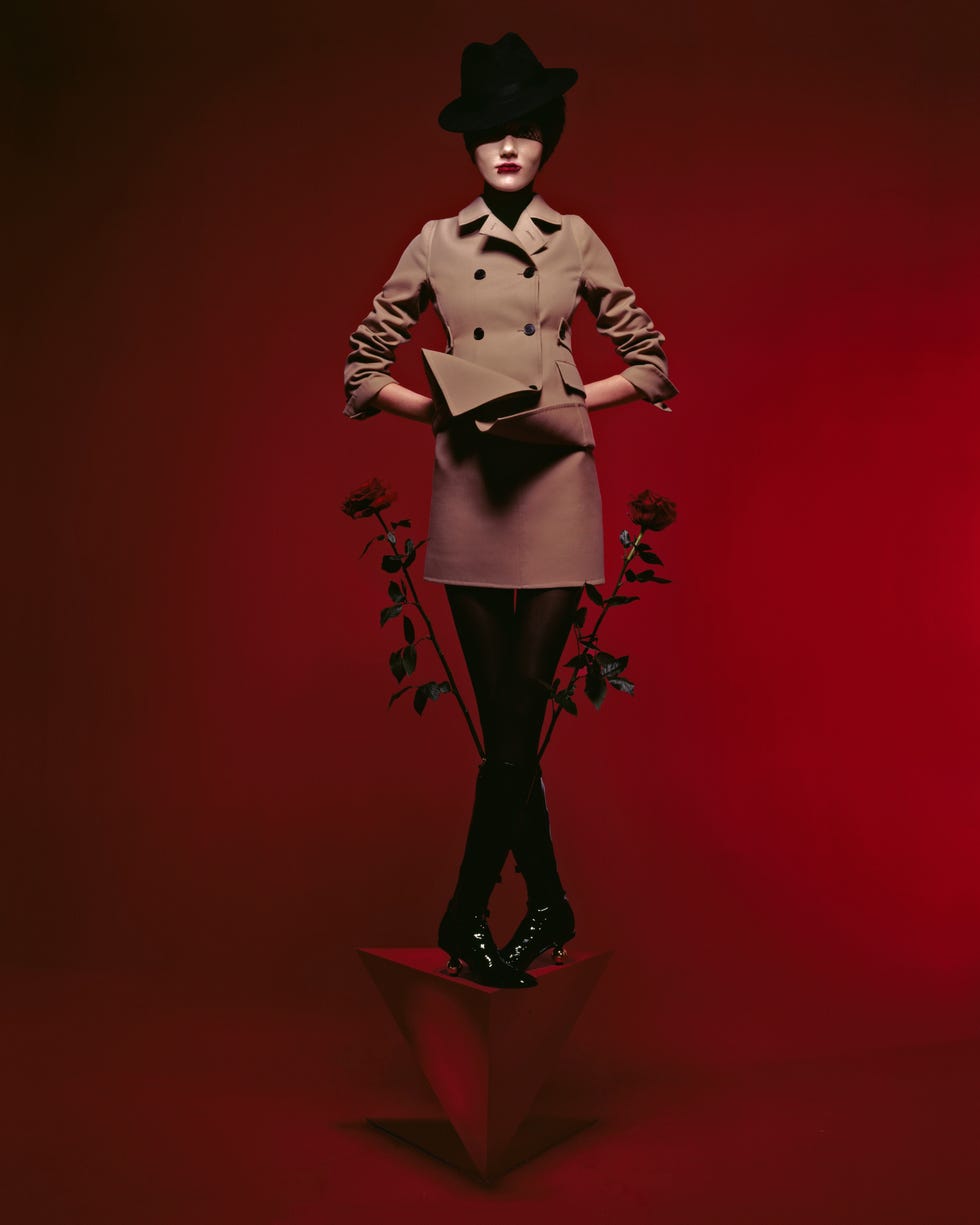 a woman in a beige trench coat standing on a red triangular block