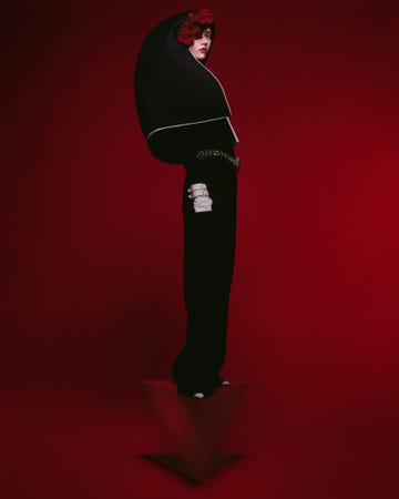 a woman wearing a black cape standing against a red backdrop