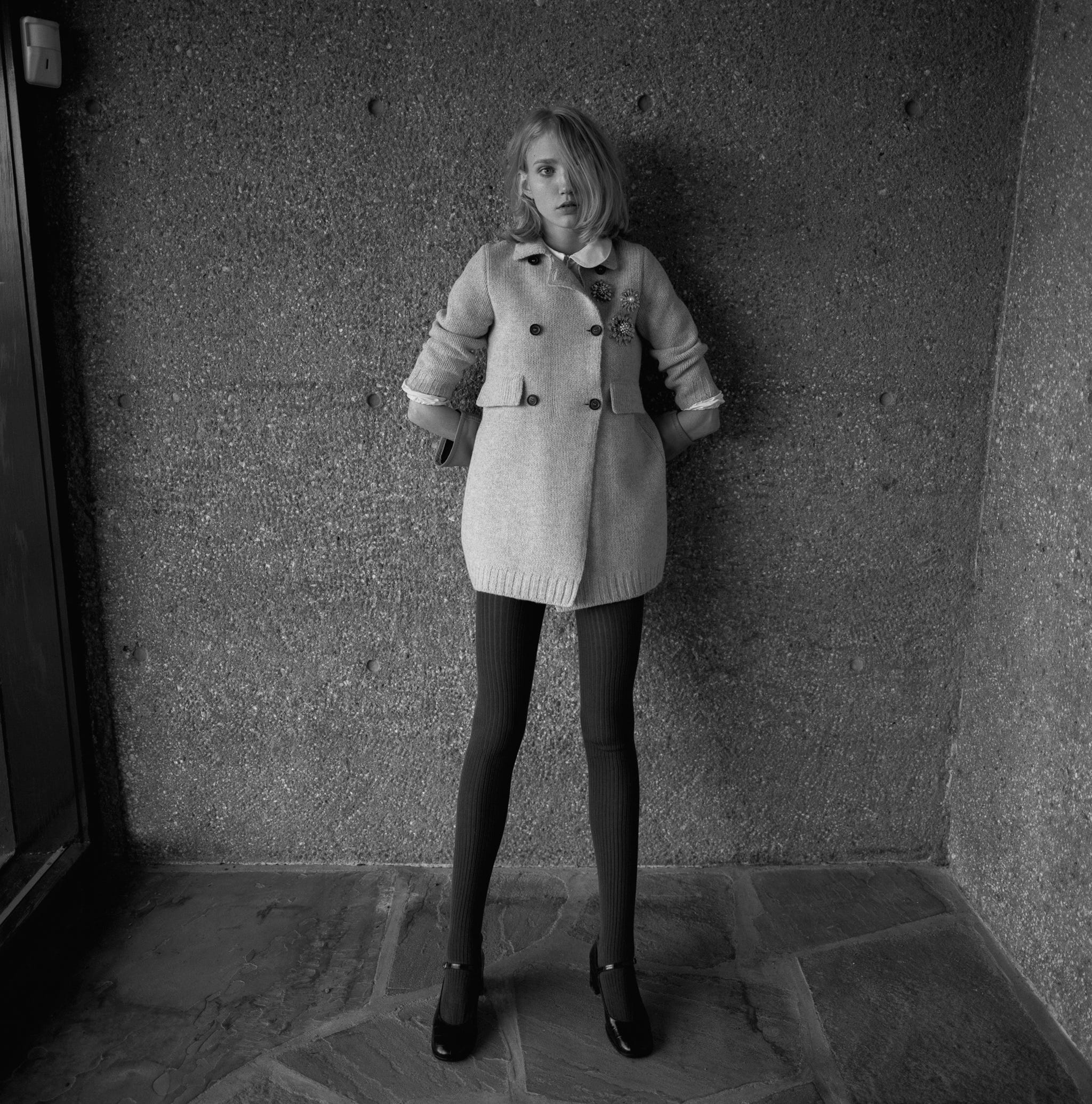 a black and white photo of a woman standing against a wall