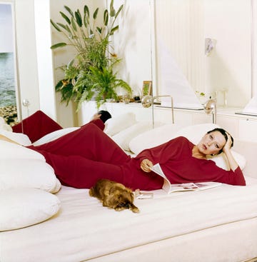 a woman in a red outfit lying on a bed with a dog