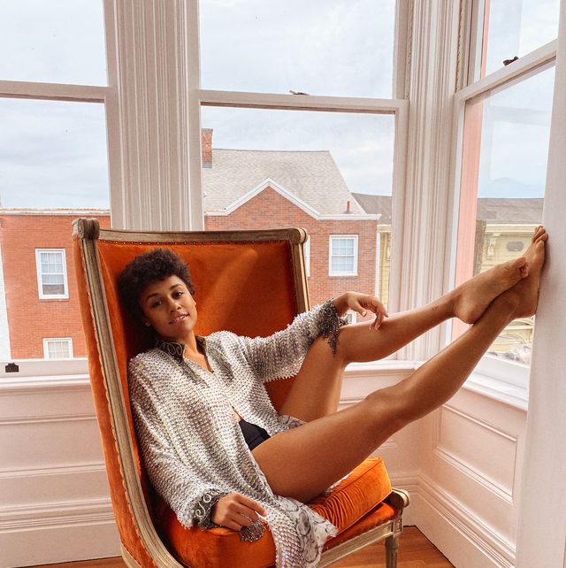 actress ariana debose sits in orange chair with legs propped on wall