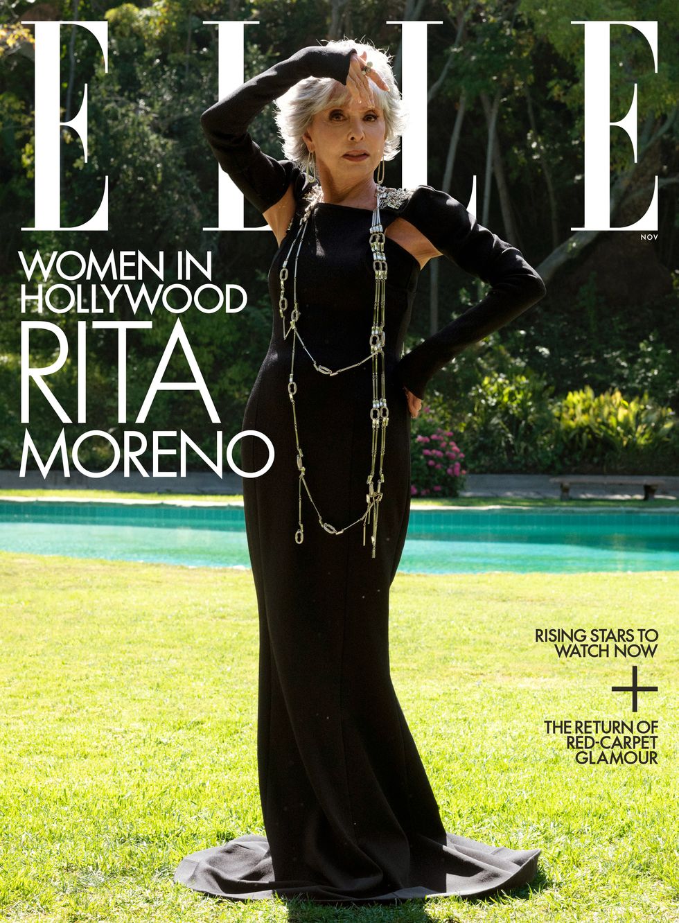 rita moreno stands on grass in front of a swimming pool wearing a dark gown