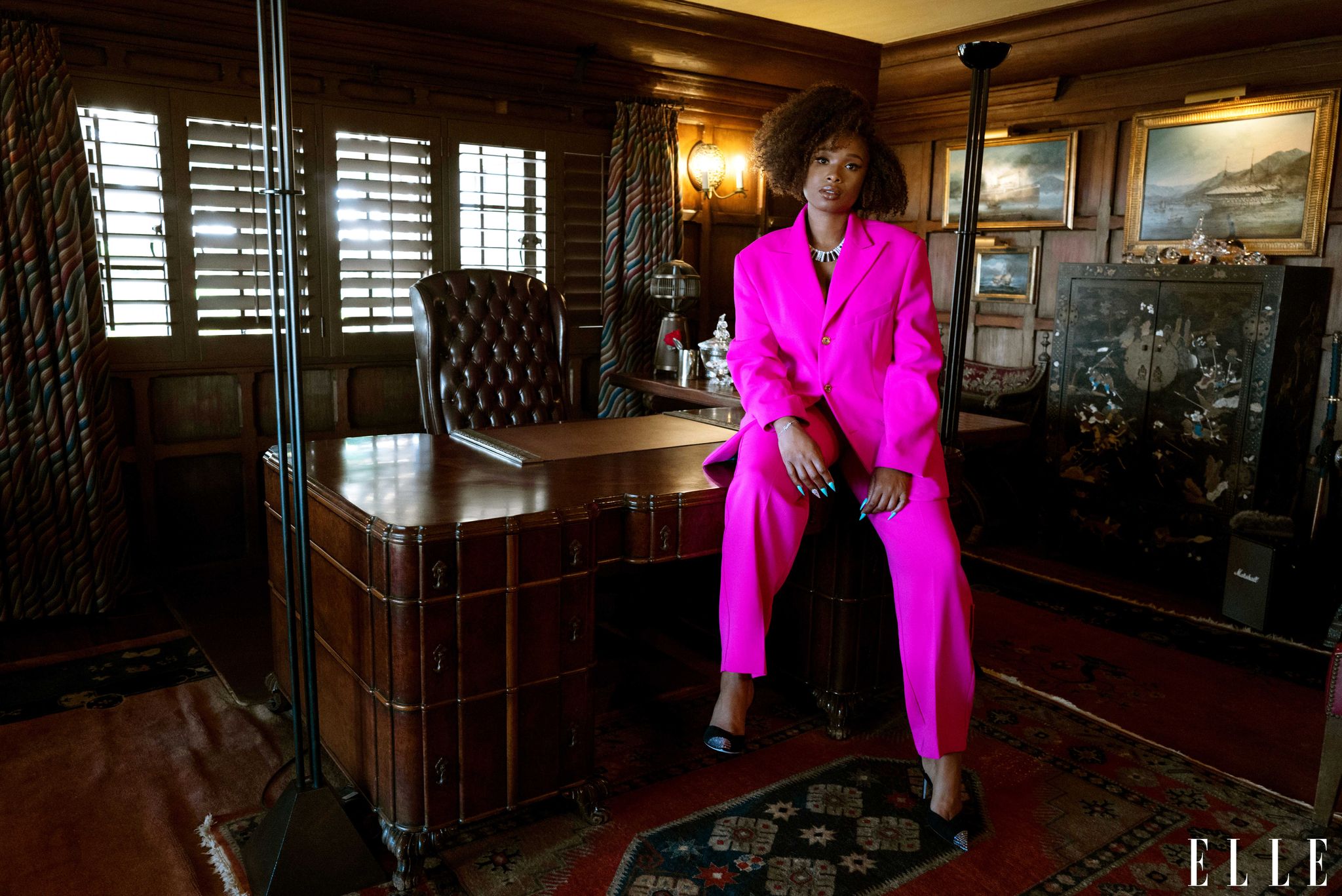 jennifer hudson wears a hot pink suit, sitting on a desk within an office