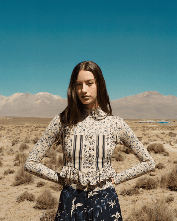 a brunette woman in a floral top standing against a desert backdrop