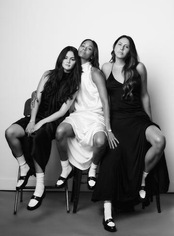 three individuals seated on stools wearing black and white dresses and socks