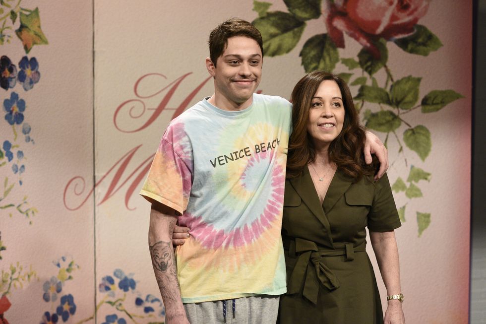 pete davidson, wearing a tie dyed t shirt with the words venice beach on it, smiles and places his left arm around the shoulder of his mother amy davidson, who wears a green dress