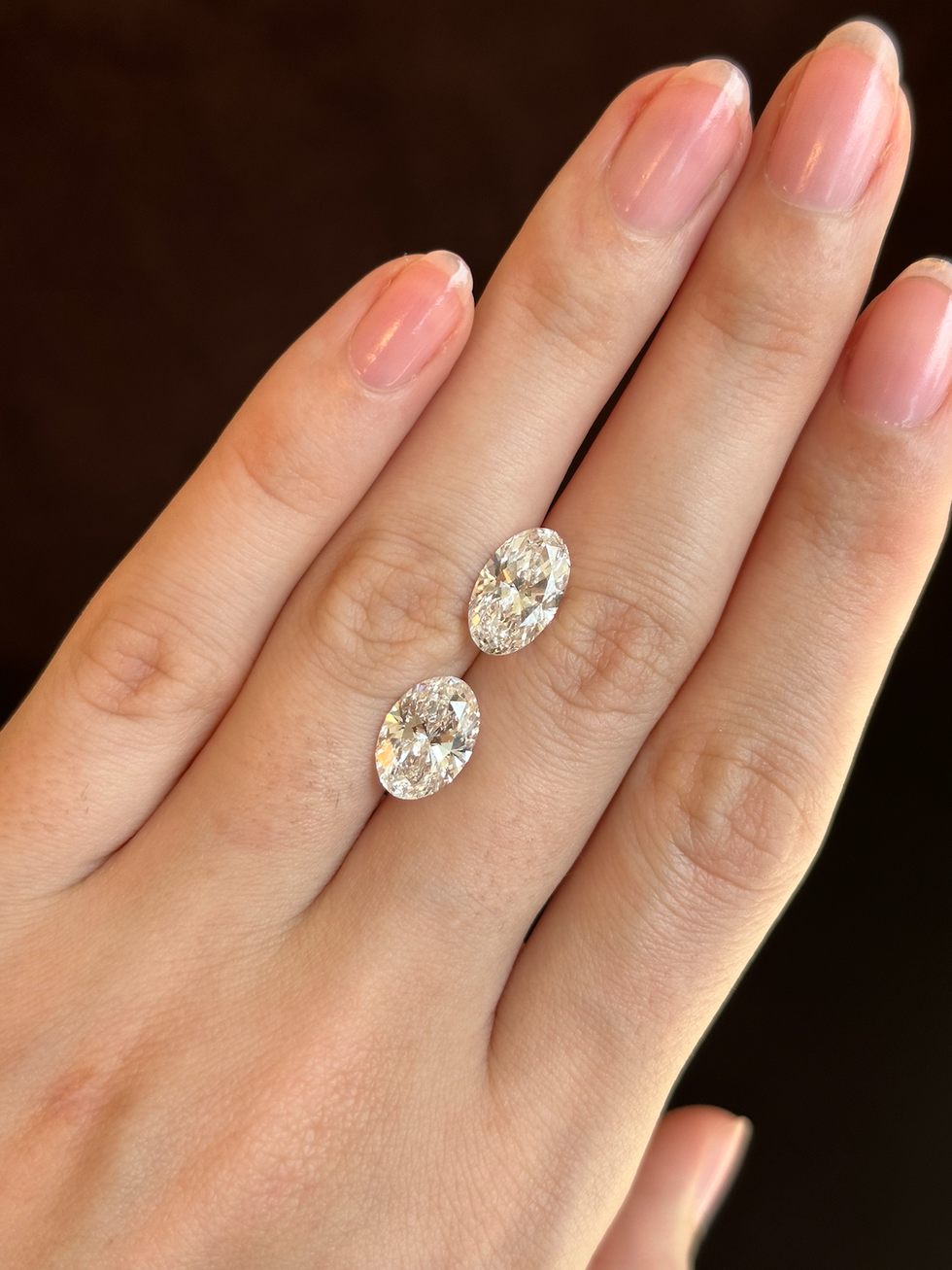 two oval diamonds, but the top stone is elongated and appears bigger than the bottom stone despite being a smaller carat weight