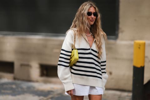 a woman wearing a striped half zip sweater with white shorts and a yellow bag on the street during new york fashion week in a roundup of cute summer outfits 2023