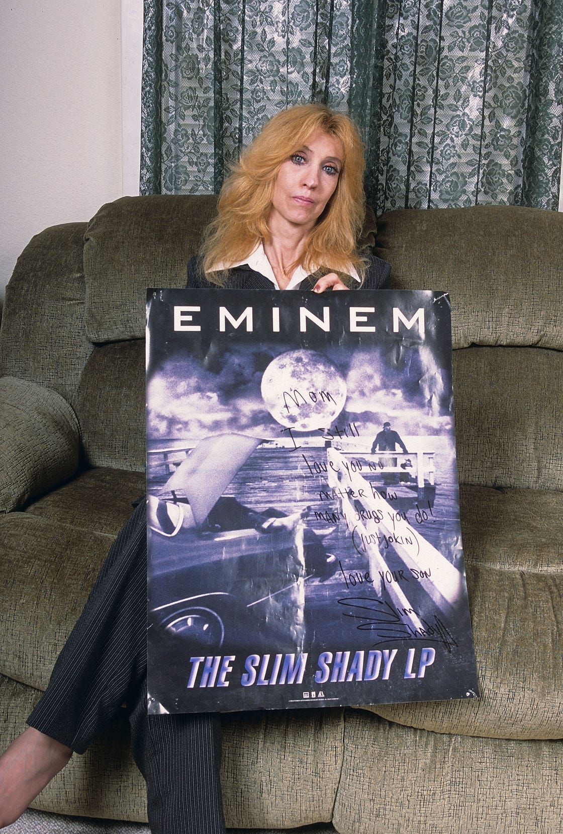 debbie mathers, the mother of rapper eminem, sitting on a couch and holding an autographed album poster