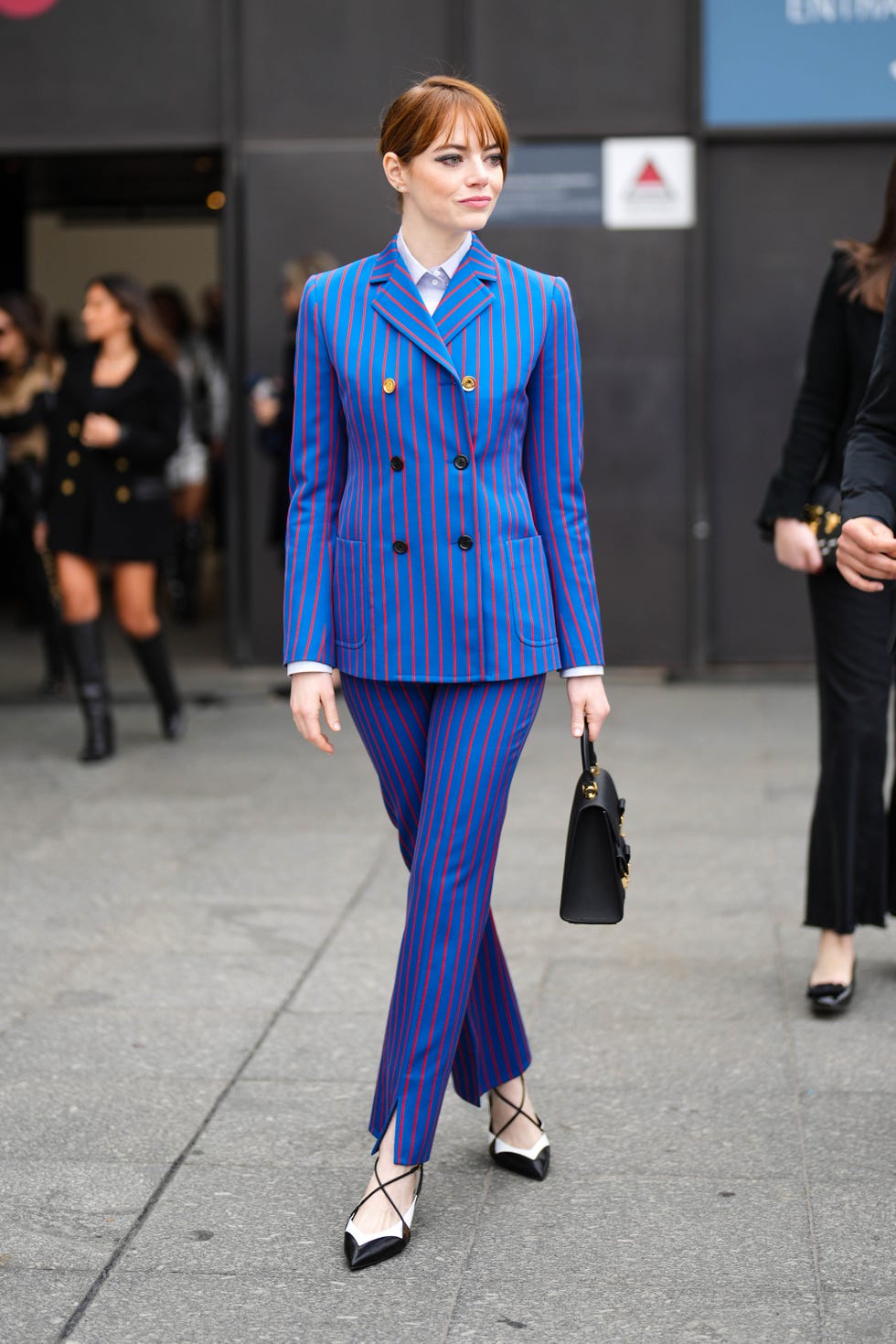 paris, france march 06 emma stone wears a white shirt, a royal blue with small red striped print pattern buttoned blazer jacket, matching royal blue with small red striped print pattern suit pants, a black shiny leather handbag from louis vuitton, black and white shiny leather pointed heels shoes , outside louis vuitton, during paris fashion week womenswear fall winter 2023 2024, on march 06, 2023 in paris, france photo by edward berthelotgetty images