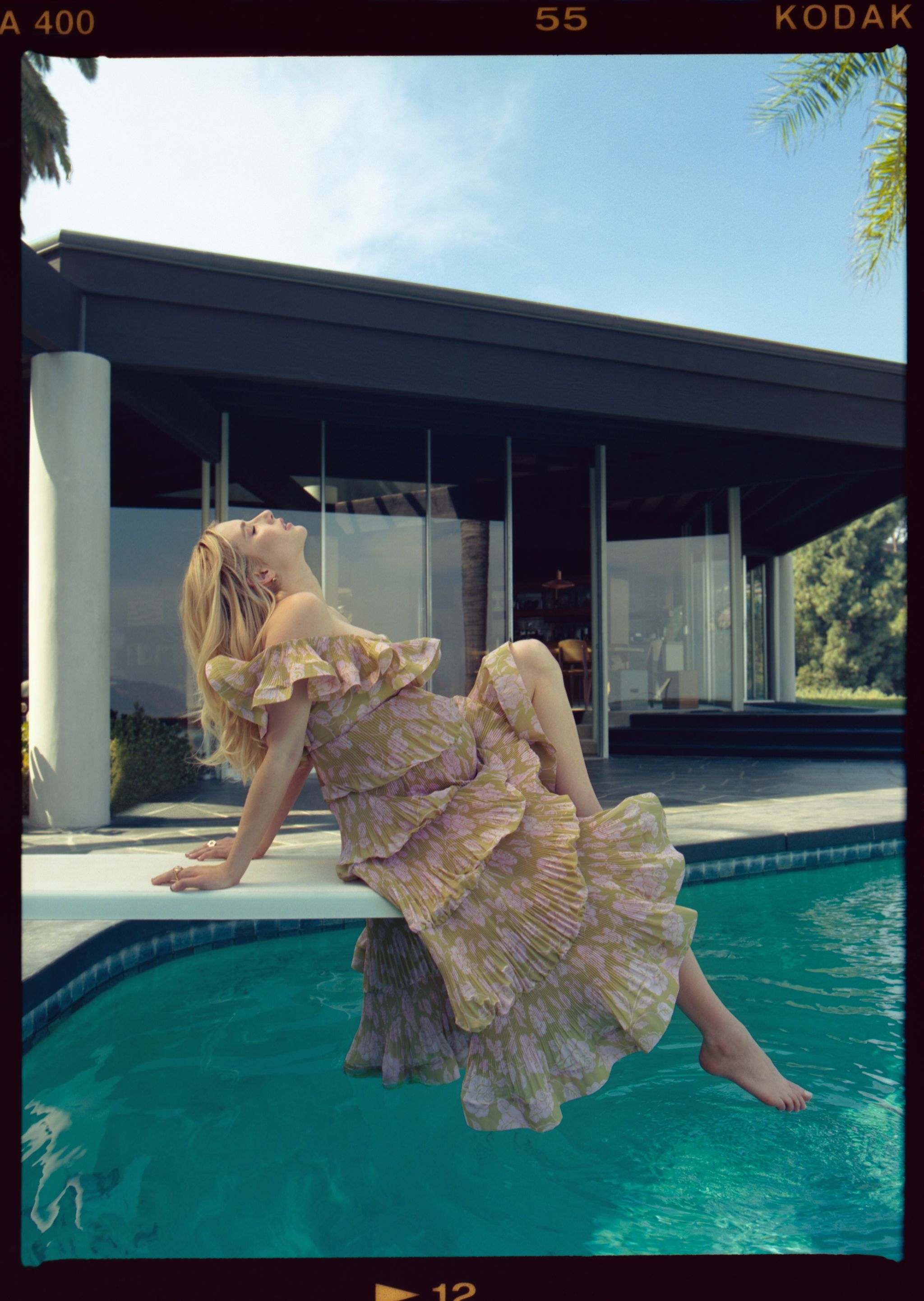 emma roberts, pregnant, wearing a green and pink rose flower dress, sitting on a diving board above pool near home looking up with closed eyes
