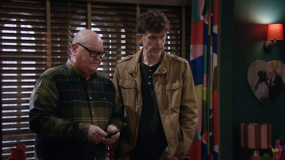 emmerdale, paddy kirk and marlon dingle indoors, with paddy in a green check shirt and marlon in a light brown jacket
