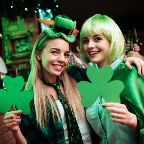 two girls in a wig and a cap are photographed in a bar they celebrate st patricks day they are having fun one girl is holding a clover