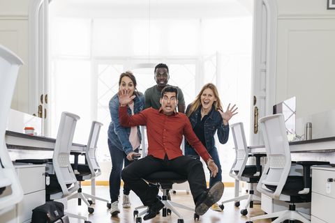 Employees pushing their boss on a swivel chair through the office