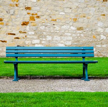 Empty Bench On Footpath Against Wall